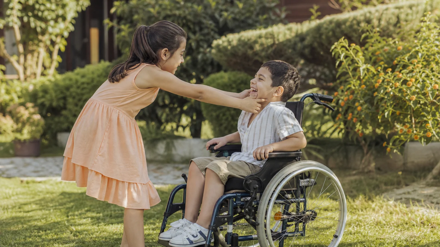 Tekerlekli sandalyedeki kardeşiyle oynayan bir kız çocuğu, özel gereksinimli bir kardeşle büyümek deneyimini yaşıyor.